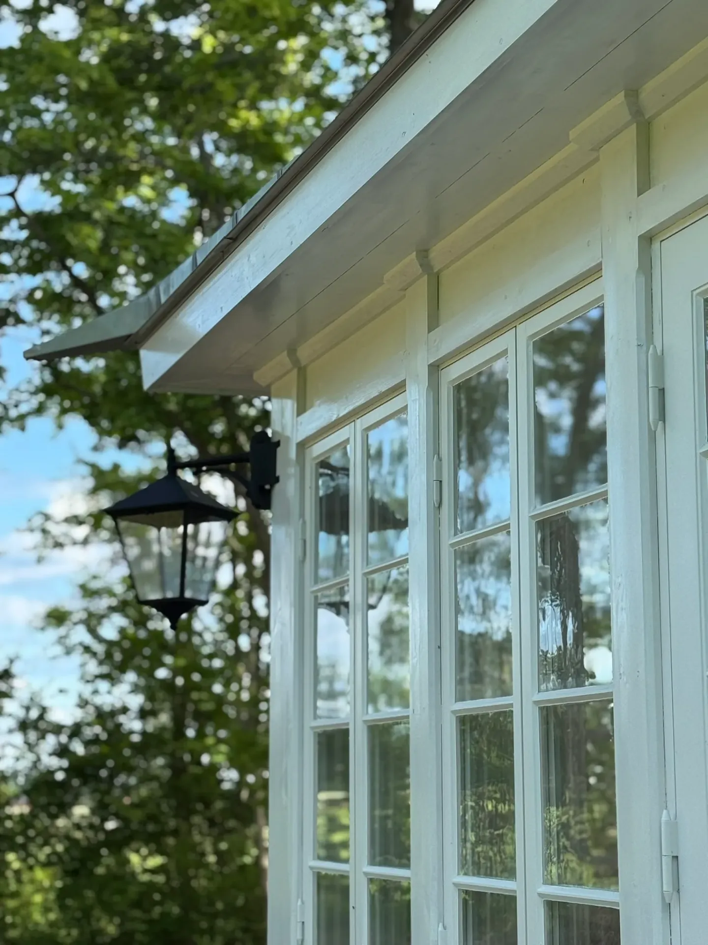 Vit glasveranda med spröjsade fönster och svart lykta