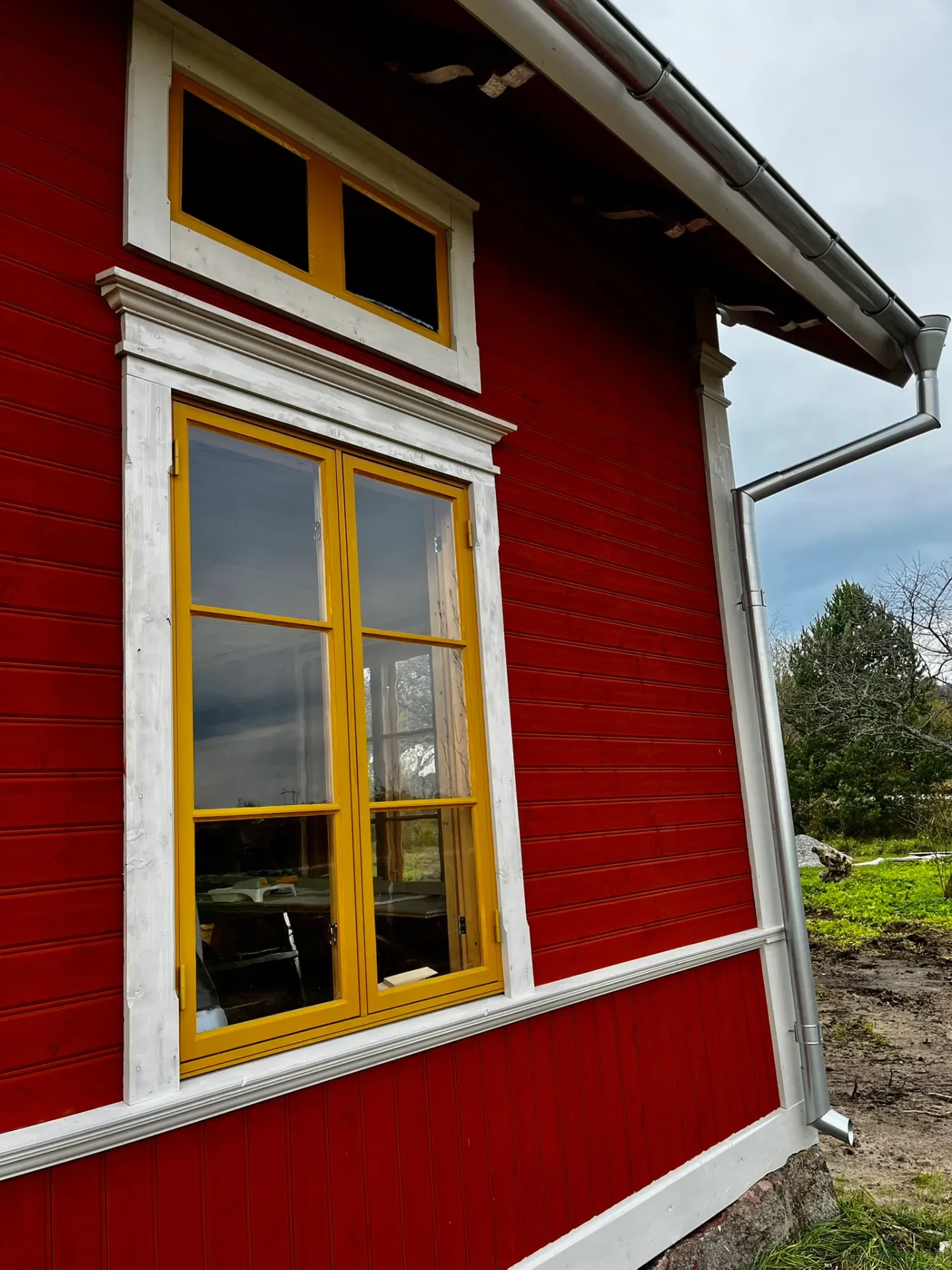 Gult spröjsat fönster med vita foder på röd träfasad