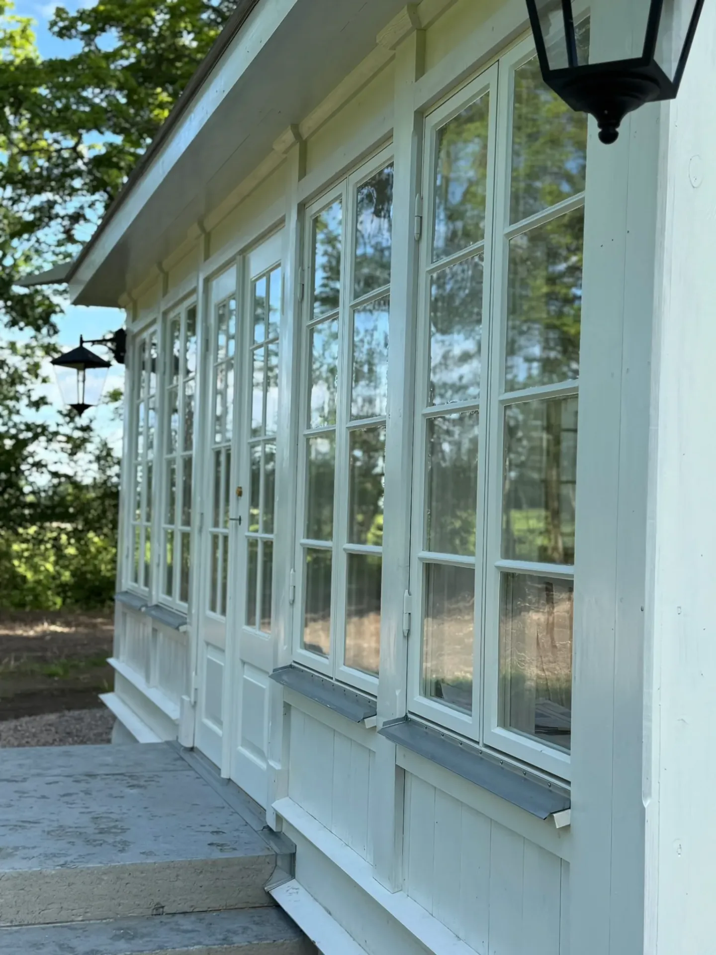 Långsida av vit glasveranda med höga spröjsade fönster