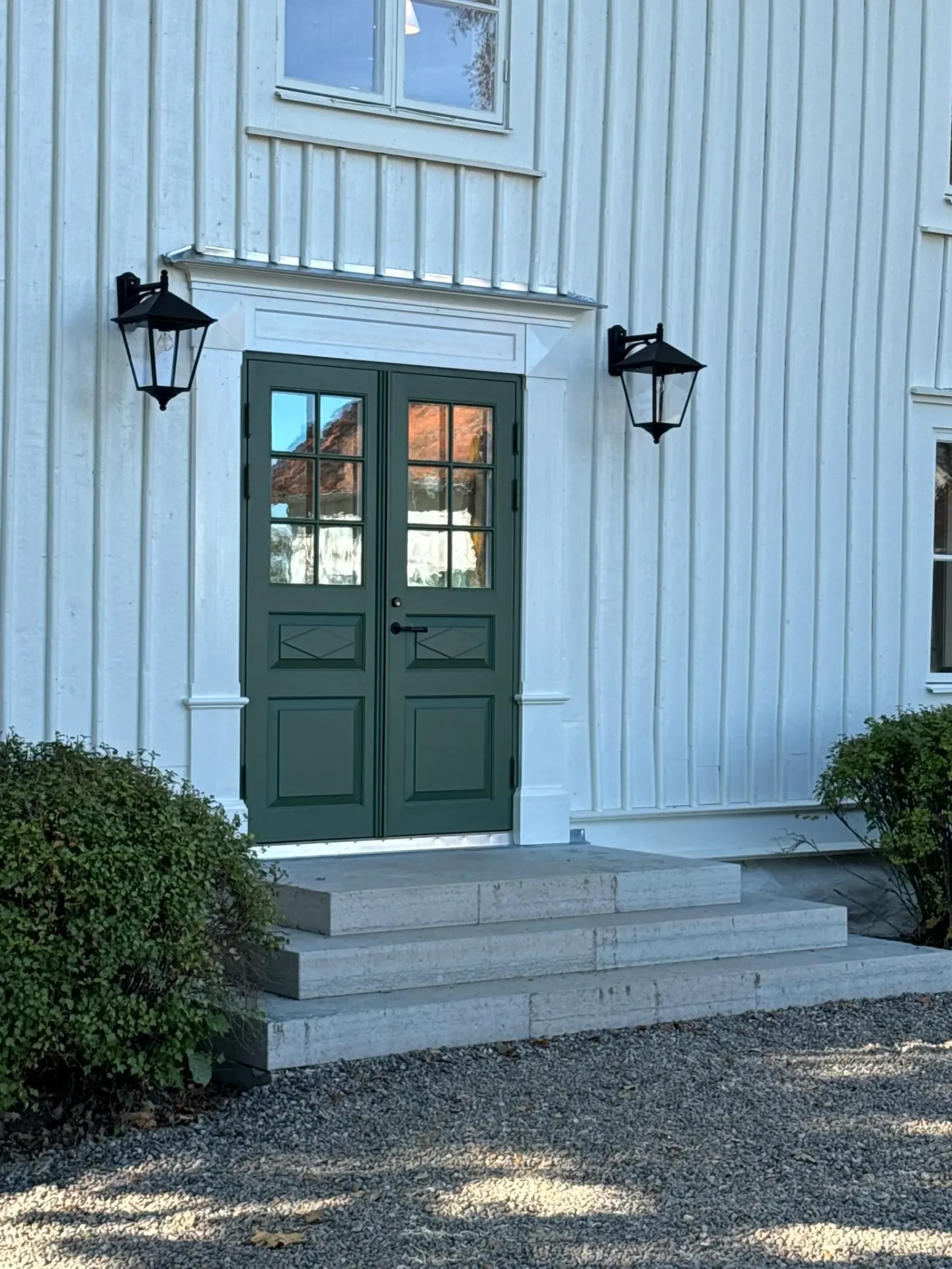Grön pardörr med glasrutor, vit fasad och stentrappa
