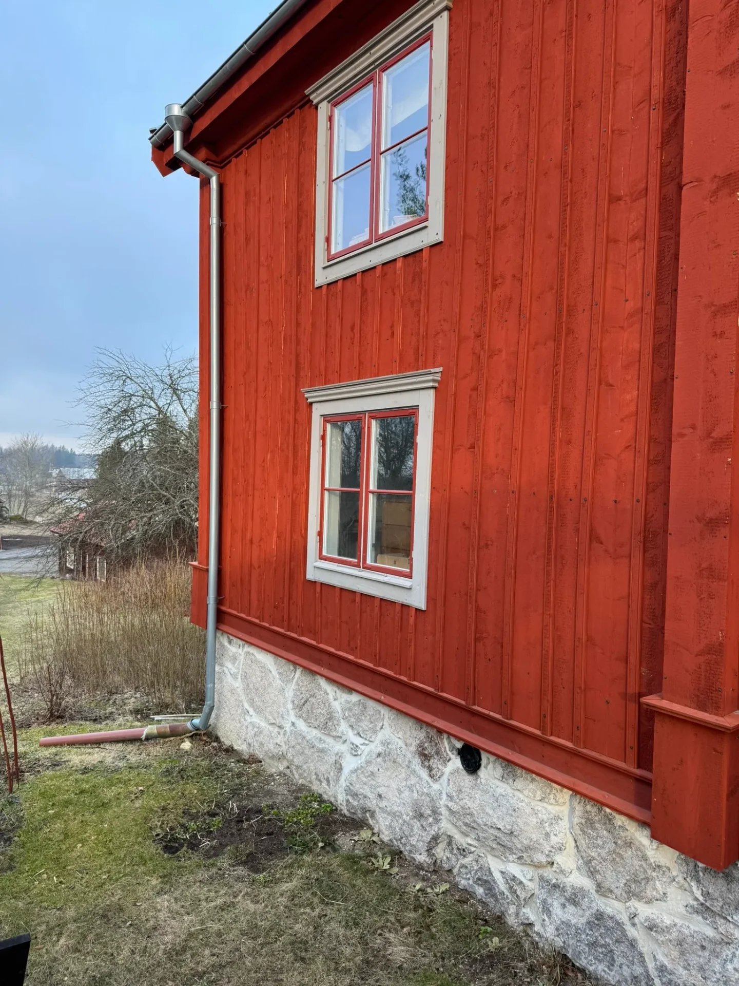 Röd träfasad med spröjsade fönster och stengrund