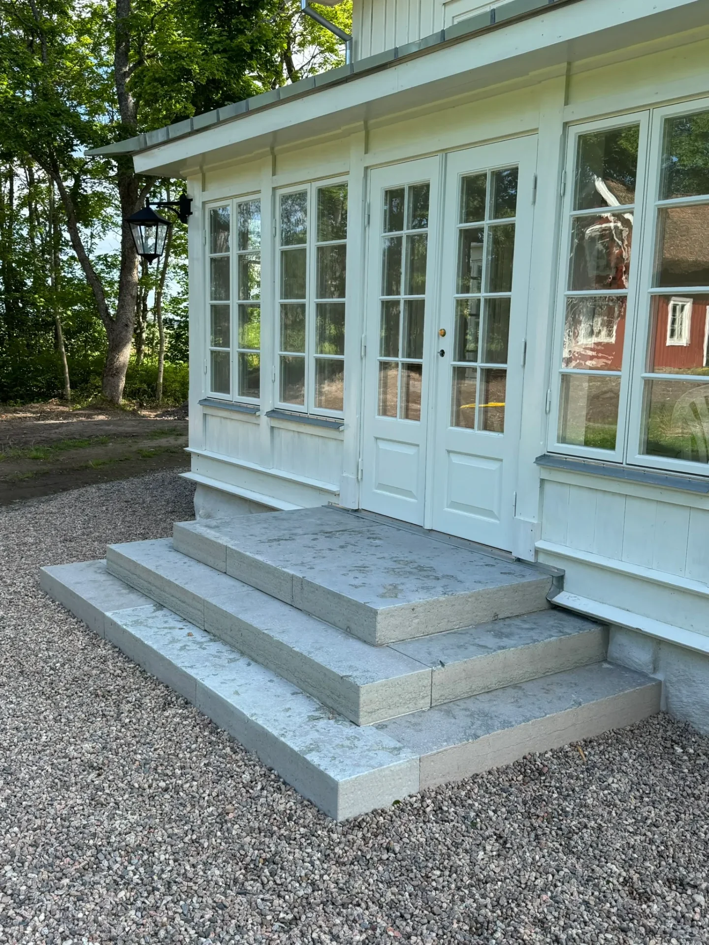 Glasveranda med stentrappa på grusplan