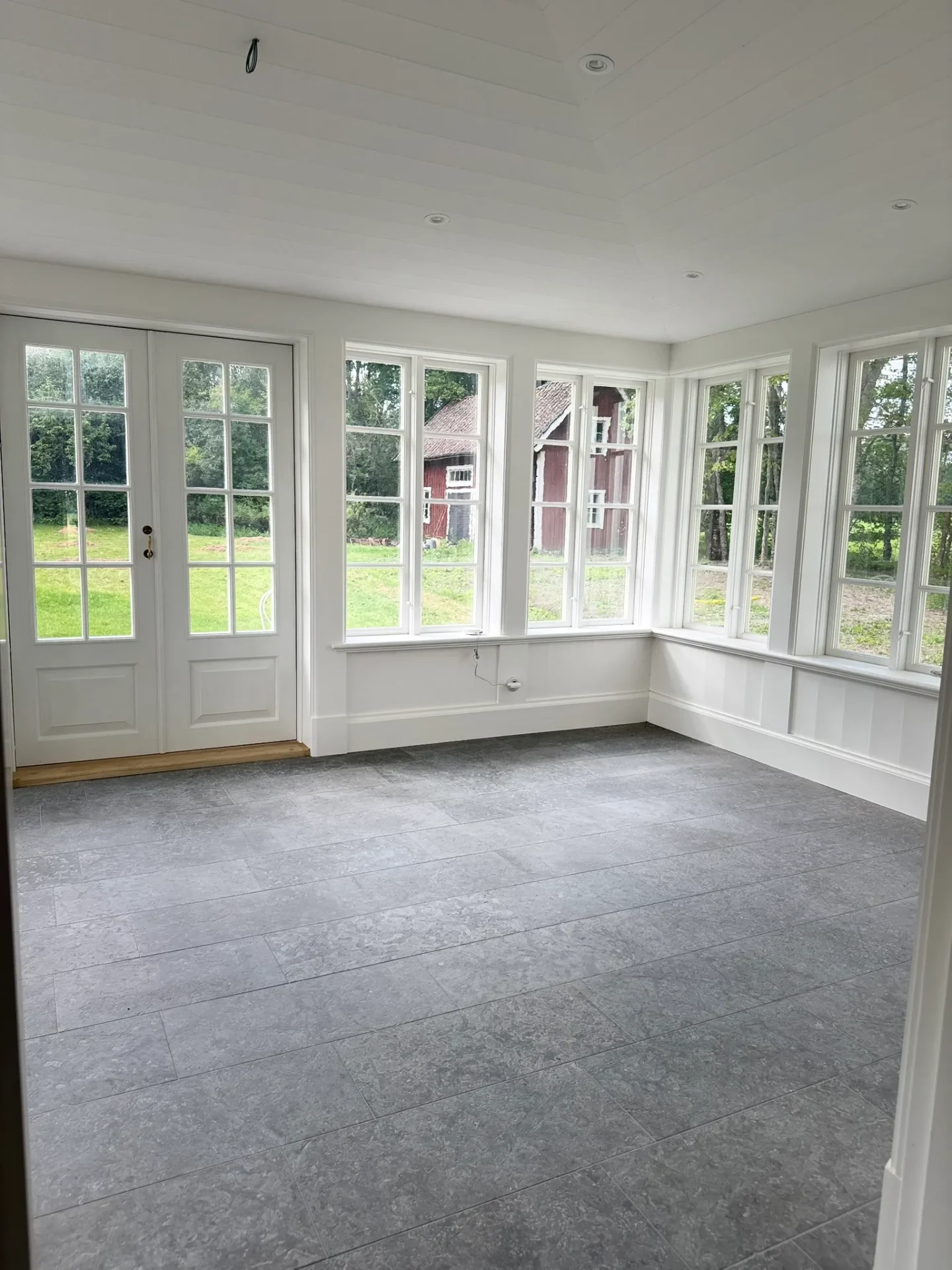 Ljus glasveranda med stengolv och spröjsade fönster